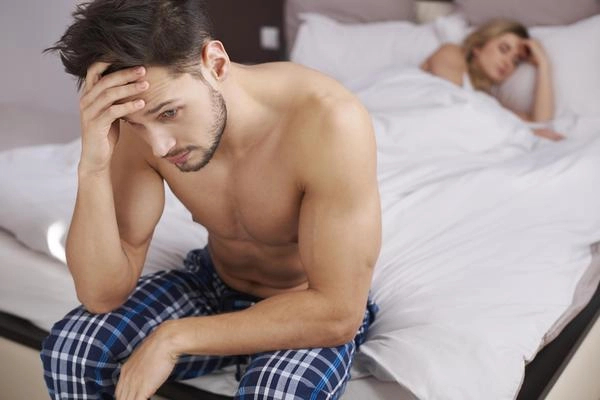 Mann sitzt frustriert im Bett bei verzögerter Ejakulation und sexuellem Leistungsdruck.