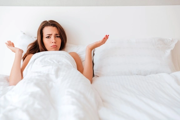 Frau liegt nach einem One-Night-Stand allein im Bett und wirkt unsicher über den Morgen danach.
