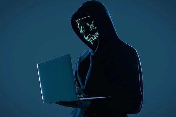 Maskierte Person mit Laptop als Symbol für anonyme Deepfake-Erstellung, Cyberkriminalität und manipulierte Inhalte.